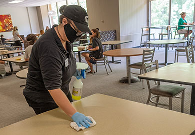 Student cleaning a table in a dining hall